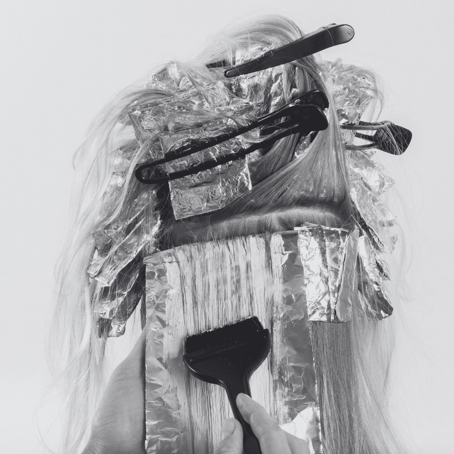 Hair being dyed with foil highlights, hair clips, and a brush.