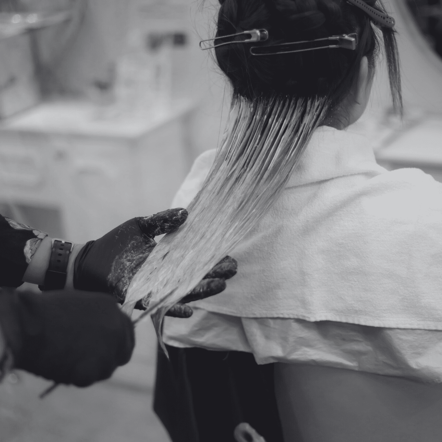 Hairdresser applying dye to woman's hair in salon setting.