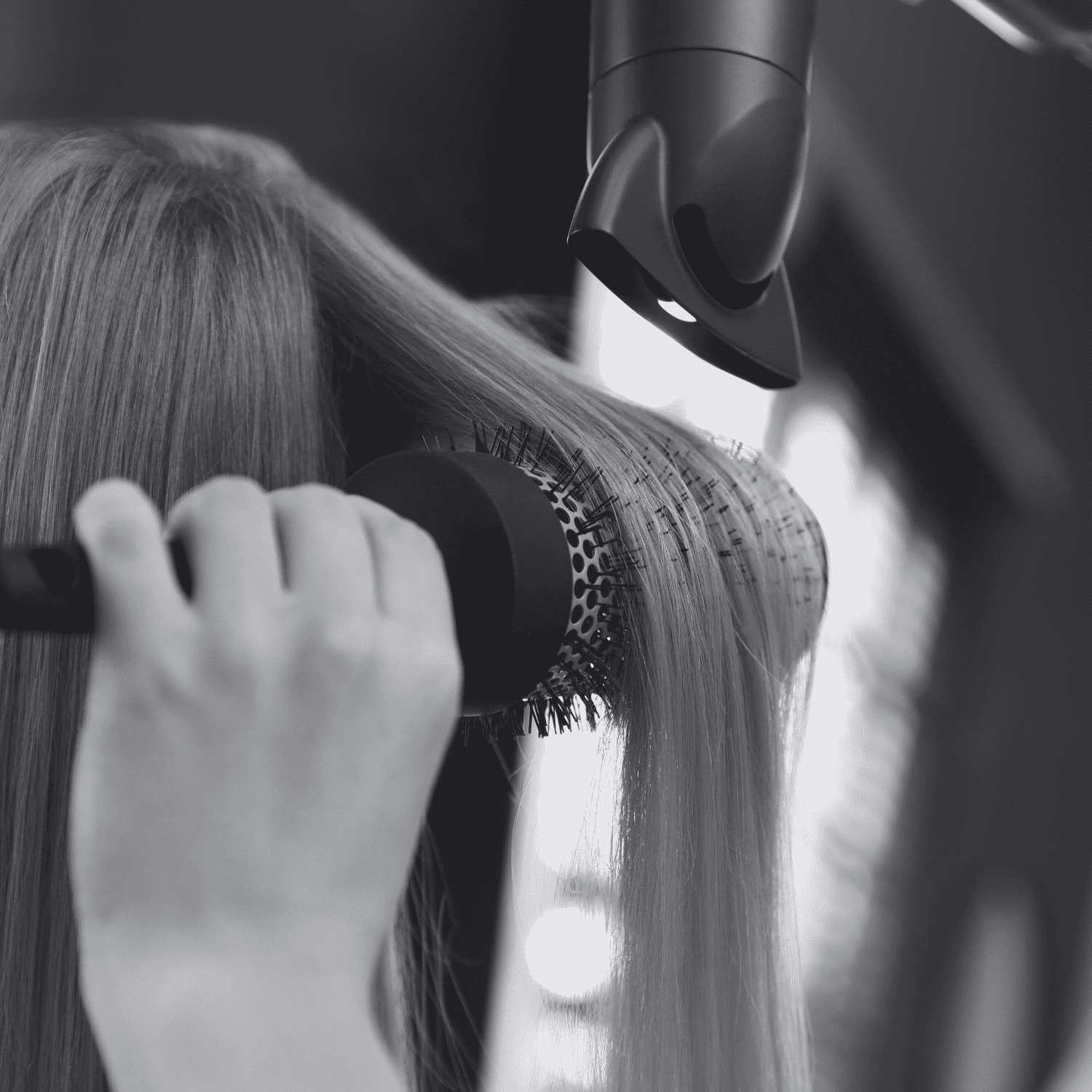 Hairdresser styling straight hair with a round brush and hairdryer.